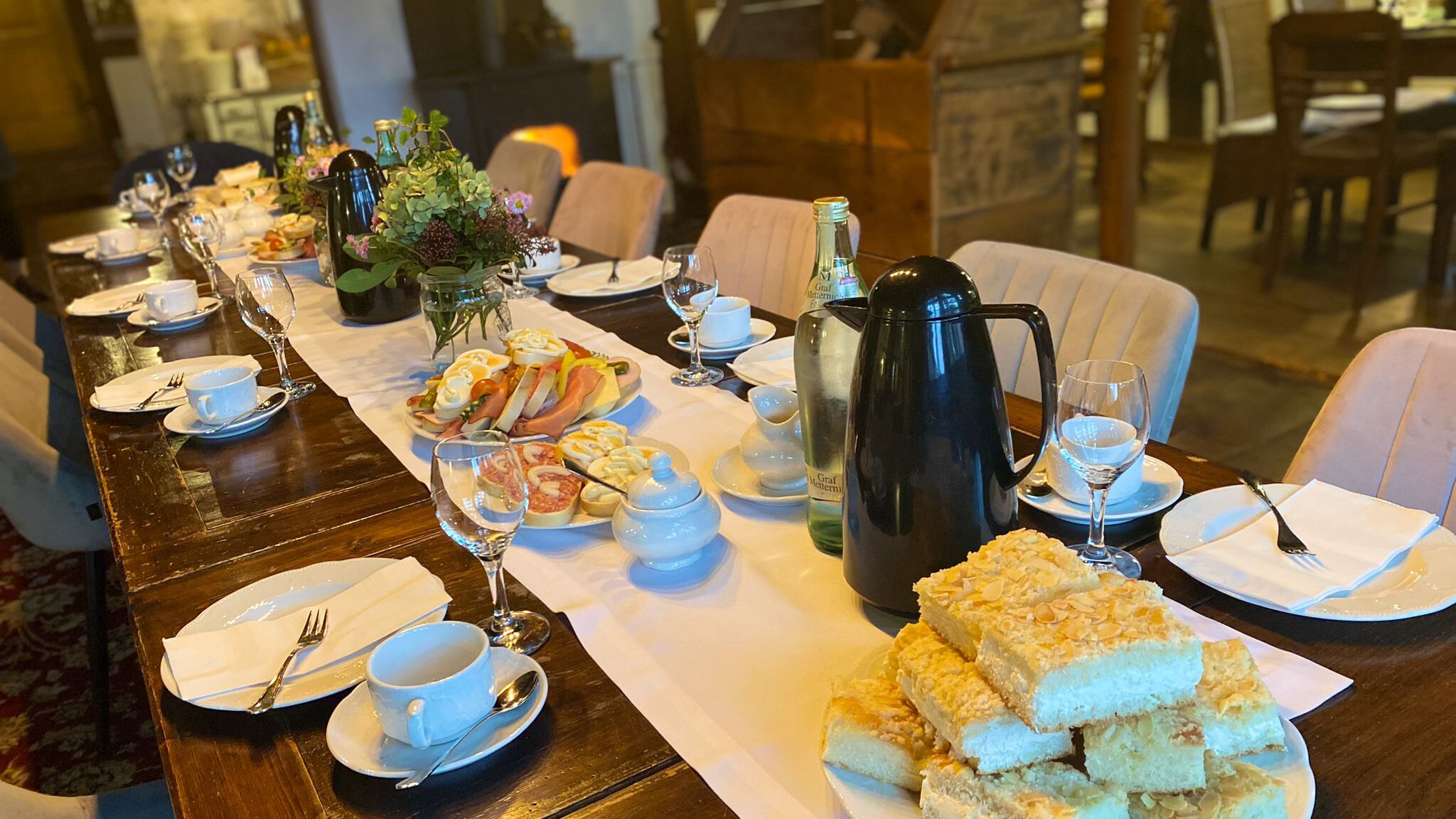 Festlich gedeckte Kaffeetafel mit Kuchen, Brot, Porzellan und Blumenschmuck im Hofcafé.