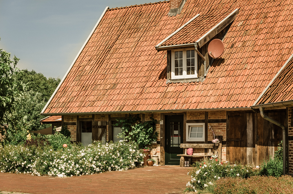 Historisches Fachwerkhaus mit rotem Satteldach und blühendem Rosenbeet auf Bussjans Hof.