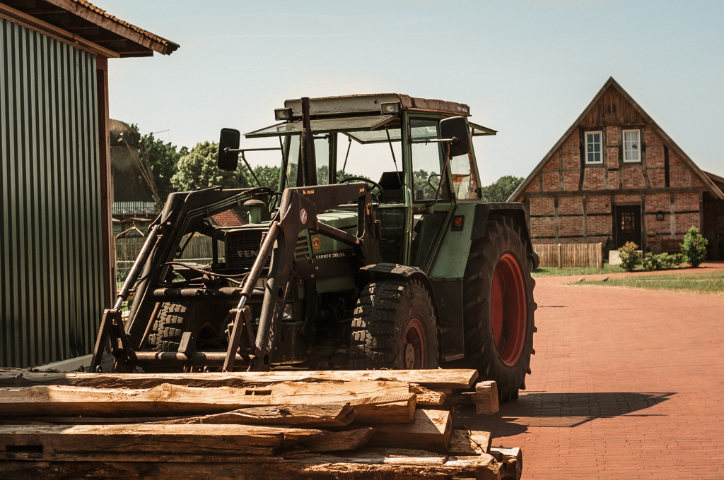 Alter Fendt-Traktor mit Holzladung vor einem traditionellen Fachwerkhaus auf dem Hof.